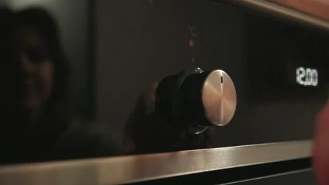 Hand turning metallic control knob on dark glass kitchen appliance with Stock-Footage 343539677