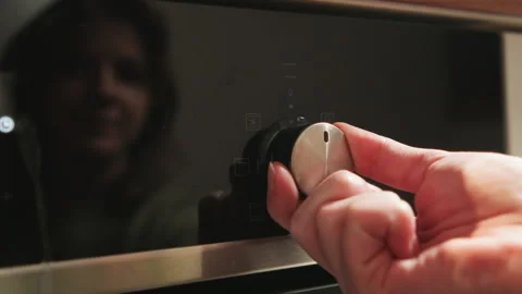Hand turning metallic knob on glossy black appliance panel with faint smiling Stock-Footage 345656713