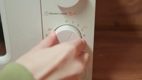 Hand turning microwave control knob on white panel beside wooden countertop with Stock Footage 343536960