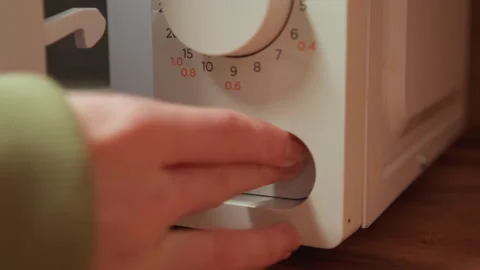 Hand turning microwave timer dial on white appliance casing above wooden Stock Footage 343535599