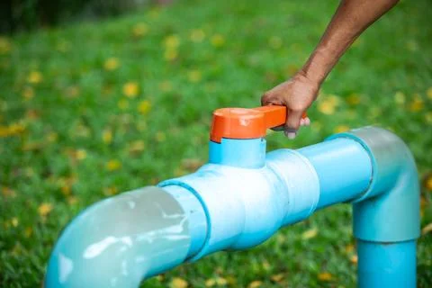 Hand turning orange valve handle on blue PVC water pipe outdoors Stock Photos