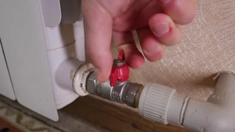 Hand Turning Red Valve to Adjust Temperature on Heating Radiator Pipe Stock Footage 339212097