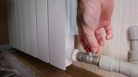 Hand Turning Red Valve on White Radiator to Adjust Home Heating System Stock Footage 339212810