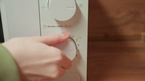 Hand turning rotary timer dial on microwave control panel in home kitchen Stock Footage 345654240