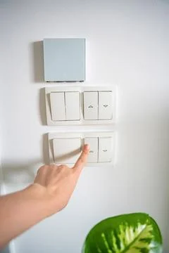 Hand turning off wall light switch beside houseplant in home interior. Energy Stock Photos