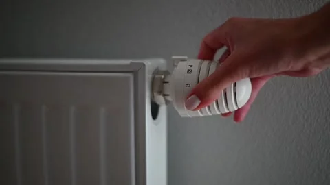 A hand turns the control knob on a radiator valve to change the heating level in Stockbeeldmateriaal 336778470