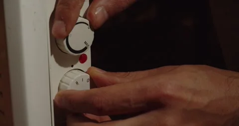 A hand turns on a convector with toggle switches and a light indicator. Heating Stock Footage 312146680