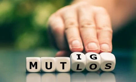 Hand turns dice and changes the German word "mutlos" ("discouraged") to "muti Stock Photos