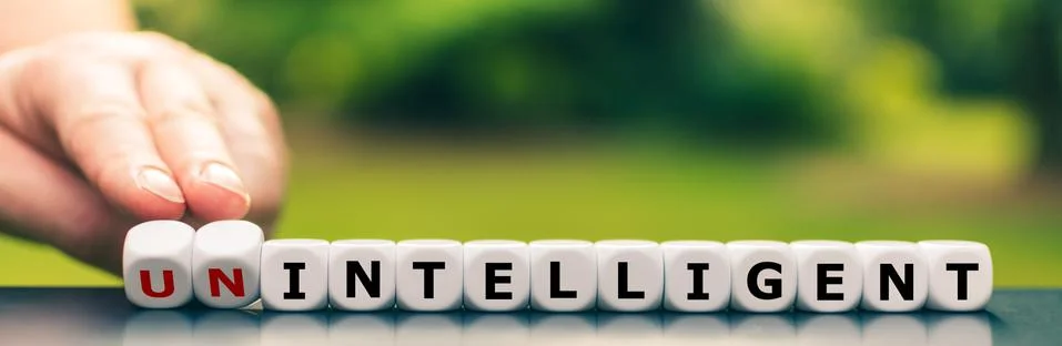 Hand turns dice and changes the expression "unintelligent" to "intelligent". Stock Photos