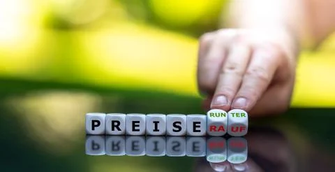 Hand turns dice and changes the German expression "Preise rauf" (price up) to Stock Photos