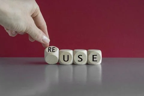 Hand turns a dice and changes the word use to reuse. Beautiful red background Stock Photos