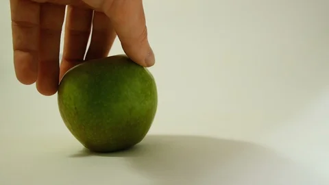 A hand turns a green apple with an incised bloody skull and a stuck syringe, a Stock Footage 98294553