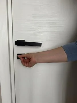 Hand turns a key to lock or unlock a white wooden interior door. Stock Photos