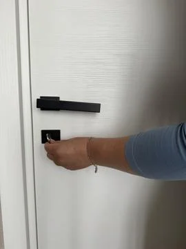 Hand turns a key to lock or unlock a white wooden interior door. Stock Photos