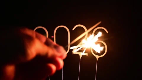 Hand with two glowing sparklers moving around unlit 2026 digits on dark bac.. Stock Footage 316985513