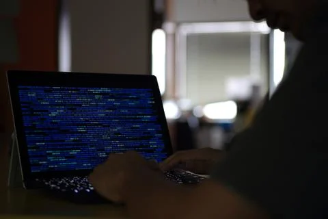 Hand typing on Laptop computer Keyboard side view. screen displaying blue dar Stock Photos