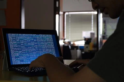 Hand typing on Laptop computer Keyboard side view. screen displaying blue dar Stock Photos