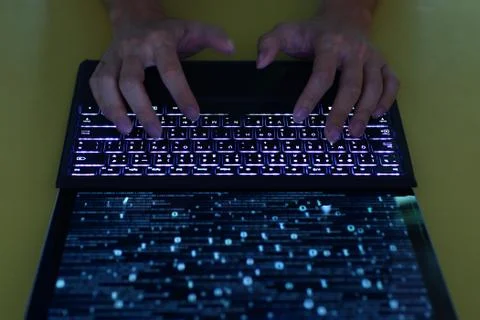 Hand typing on Laptop computer Keyboard side view. screen displaying blue dar Stock Photos