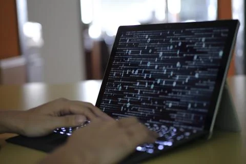 Hand typing on Laptop computer Keyboard side view. screen displaying blue dar Stock Photos