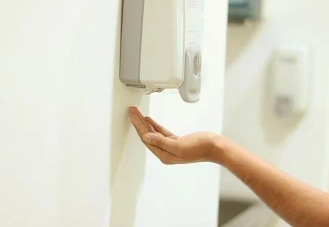 Hand under an automatic wall mounted sanitizer dispenser. Stock Photos