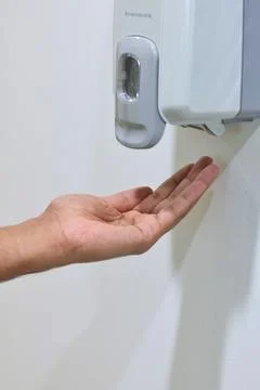 Hand under an automatic wall mounted sanitizer dispenser. Stock Photos