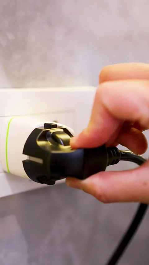 Hand Unplugging a Black Power Cable from a European Wall Socket Stock Footage 333164755
