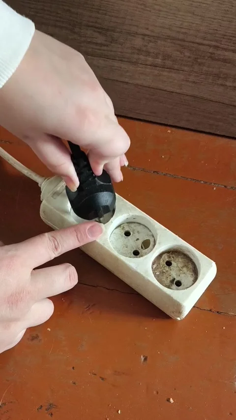 The hand unplugs the plug from the socket with an extension cord. electricity Stock Footage 325287794