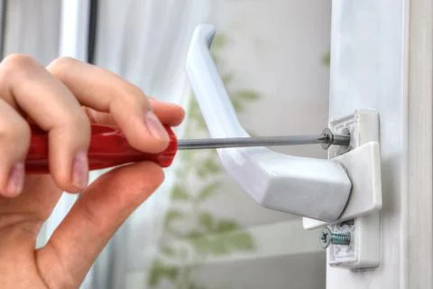 Hand unscrews the bolt, using a screwdriver, uninstall window handle. Stock Photos