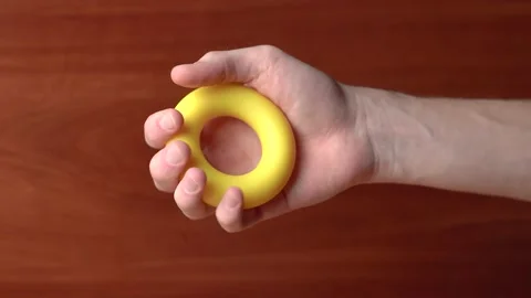 Hand unsuccessfully tries squeeze hand expander many times on wooden background Stock Footage 145563620