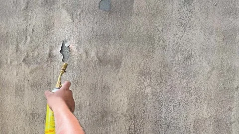 Hand Uses Blowtorch to Bubble Paint and Texture Gray Plaster Wall Stock Footage 344457323