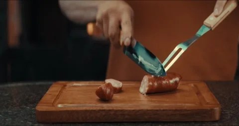 Hand uses a knife to slice sausage on wooden cutting board Stock Footage 336976081