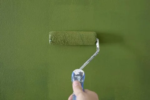 Hand uses paint roller to apply green paint to an interior wall. Concept of h Stock Photos