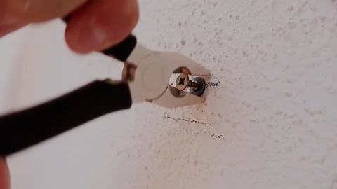 Hand uses pliers to remove a screw from a textured wall Stock Footage 345175545