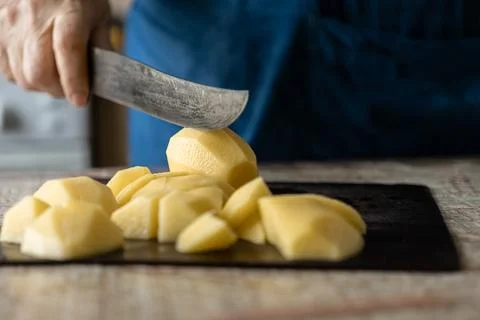 A hand uses a sharp knife to cut raw potatoes on a dark wooden board, conve.. Stock Photos