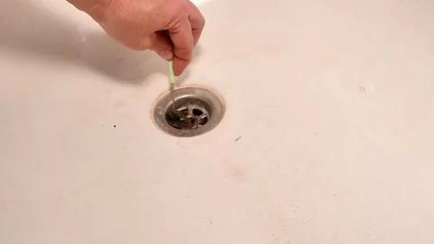 Hand uses tool to remove hair clog from drain. Stock Footage 338329868