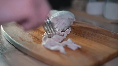 A hand uses two forks to shred cooked chicken on a wooden cutting board. The 库存影片 338301361