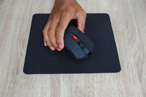 Hand Using A Black Wireless Mouse On A Wooden Desk 스톡 사진