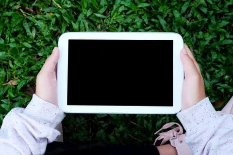 Hand using blank screen tablet over green grasses background Stock Photos