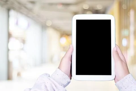 Hand using blank screen tablet over blur store with bokeh background, mock up Stock Photos