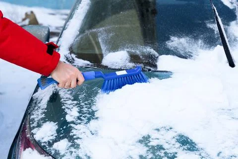 Hand using blue snow brush to clean car windshield in winter, close up view.. Stock Photos