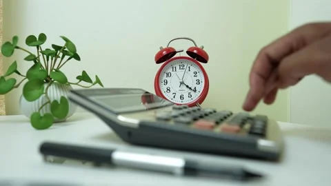 Hand Using Calculator with Alarm Clock on Desk Stock Footage 317737445