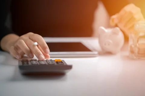 Hand using calculator and putting coin to piggy bank, Saving money and calcul Stock Photos