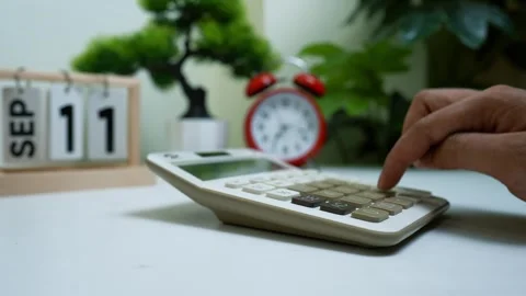 Hand using calculator on desk with calendar and clock Stock Footage 318056633