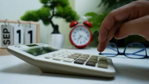 Hand using calculator on desk with calendar and clock Stock Footage 318056640