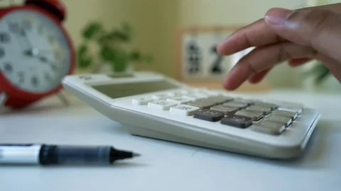 Hand Using Calculator on Desk with Pen and Clock Stock Footage 317737077