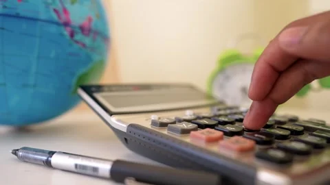 Hand using a calculator with a pen, globe, and clock in the background Stock Footage 318056807
