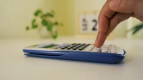 Hand using a calculator on a white desk with a laptop and a small plant Stock Footage 317737073