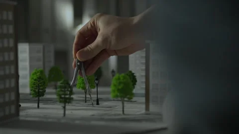 A hand using a compass to design a miniature urban landscape with trees and Stock Footage 287957976