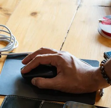 A hand using a computer mouse on a wooden desk, highlighting everyday compu.. Stock Photos