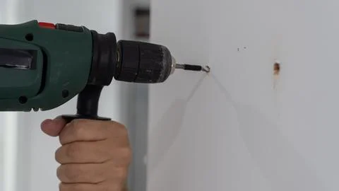 Hand Using Cordless Drill to Drill Hole in White Wall 스톡 사진